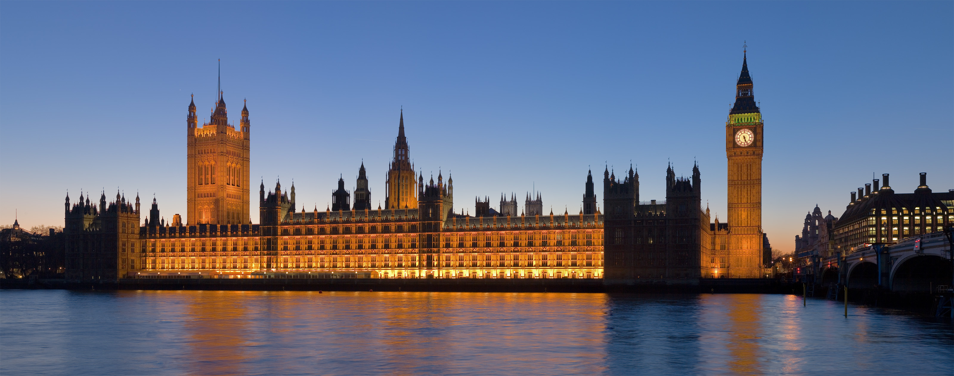 The illuminated Palace of Westminster seen across the River Thames at dusk.